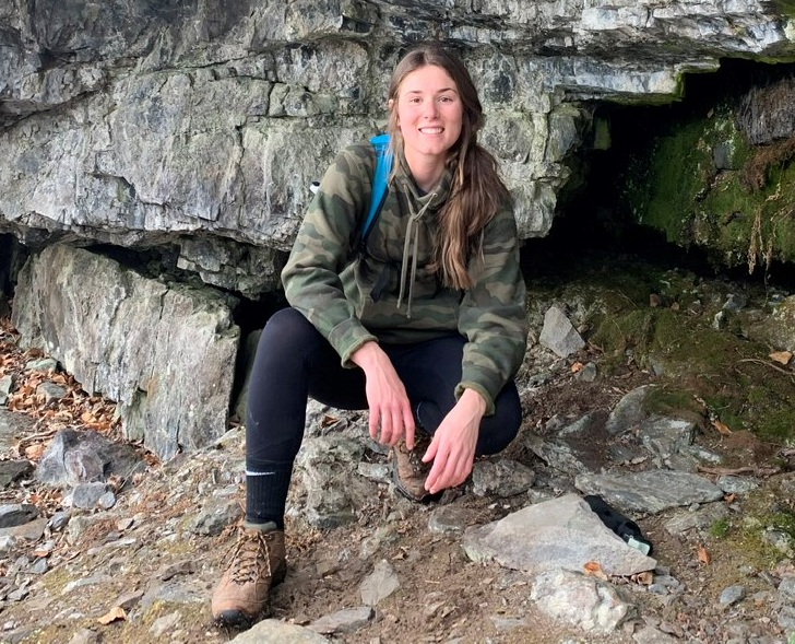 Christina Medwid wearing hiking gear and crouching with rocks in the background