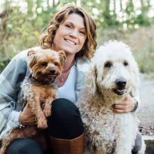 A smiling Carie Eldon poses outdoors with two dogs